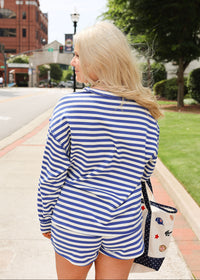 Woman in a blue and white striped outfit walking on a sidewalk with a tote bag.