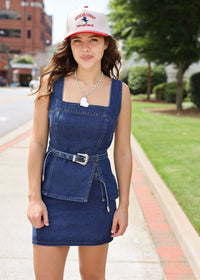 Woman wearing a denim dress and a cap with a logo on a sidewalk.