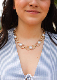 Woman wearing a gold chain necklace with pearl-like beads.