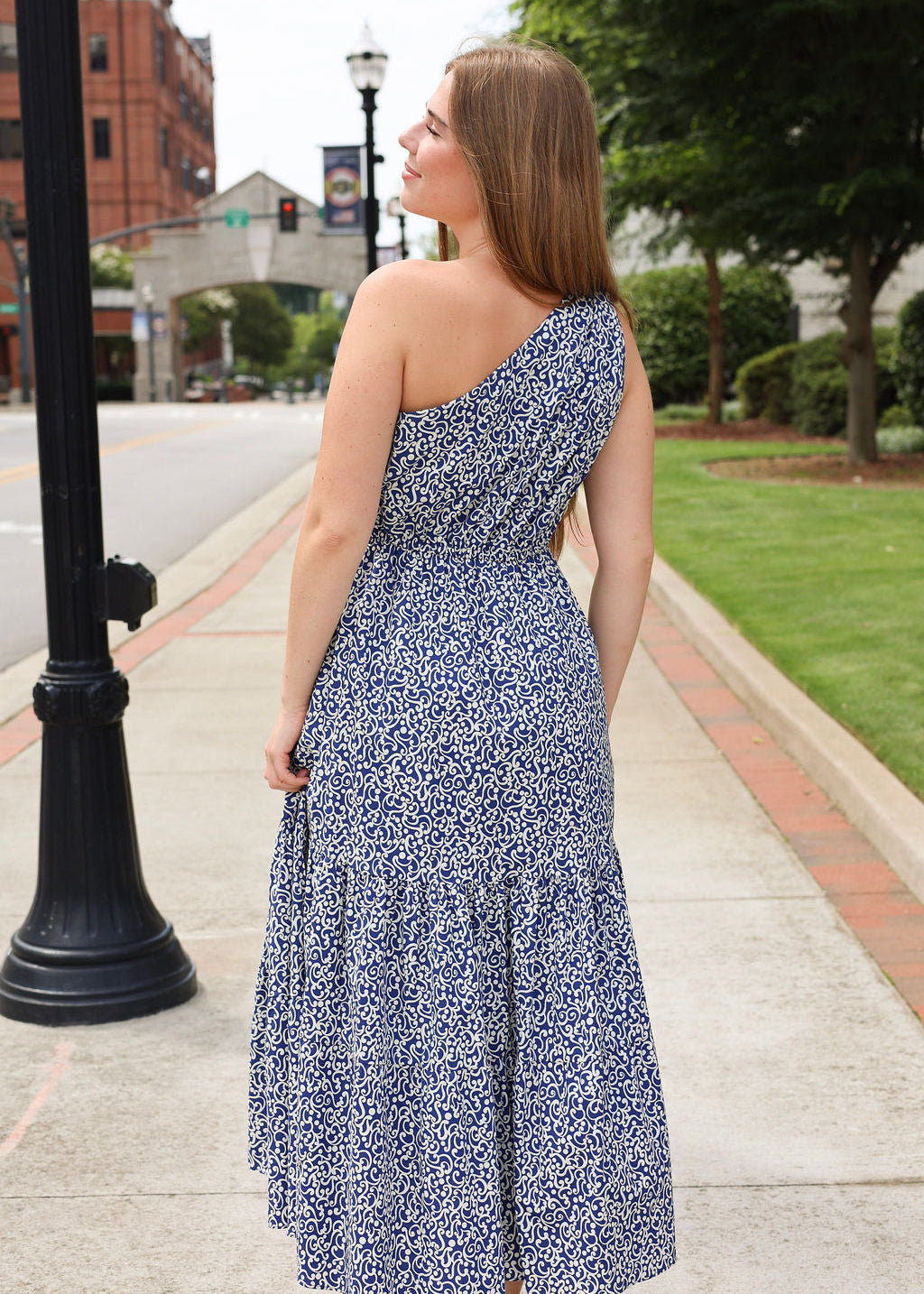 Woman in a blue floral dress standing on a sidewalk with a cityscape background