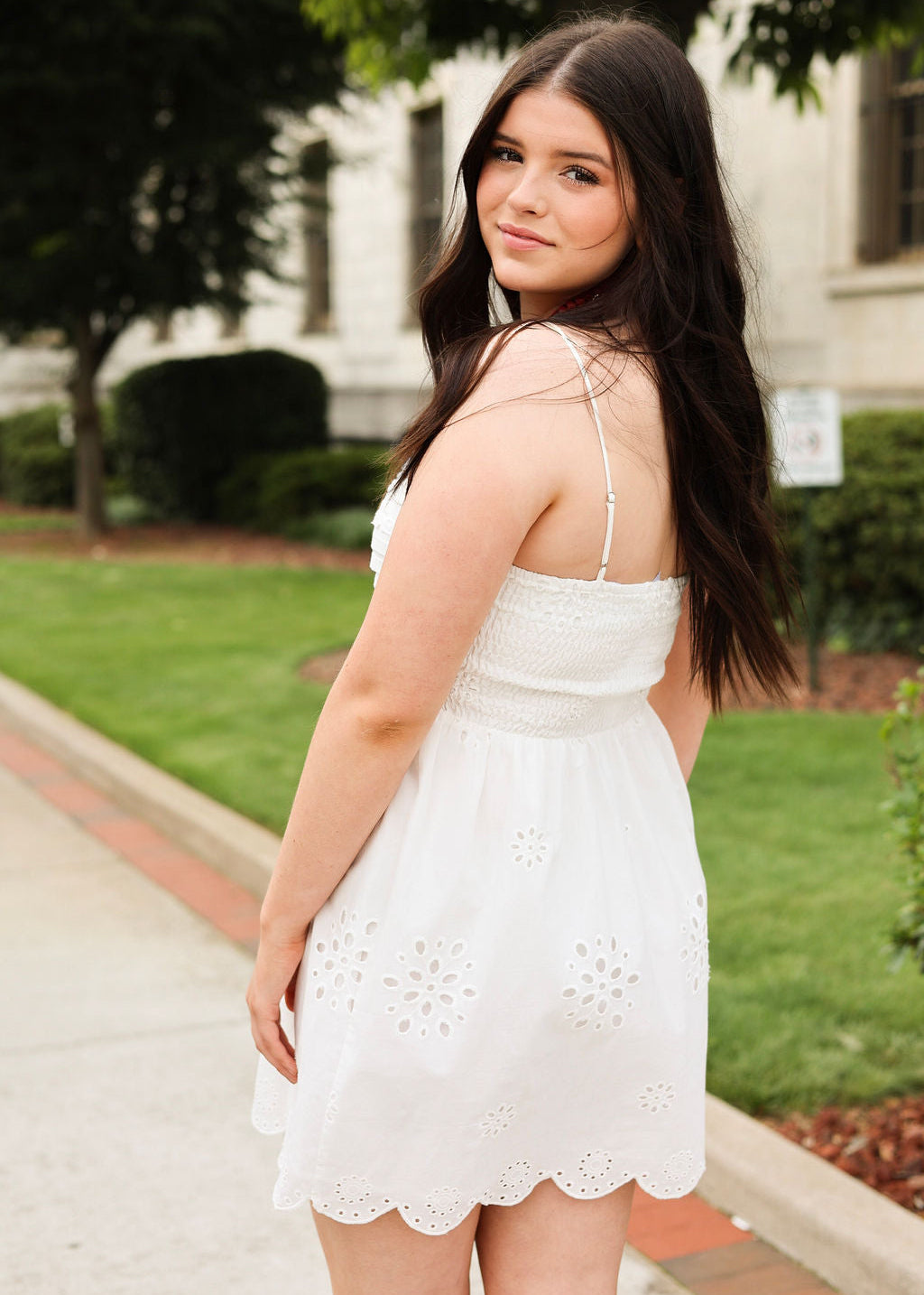 Woman in a white dress standing outdoors with greenery in the background