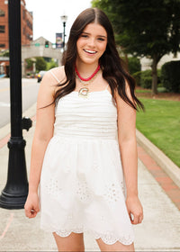 Woman in a white dress with red jewelry standing on a sidewalk
