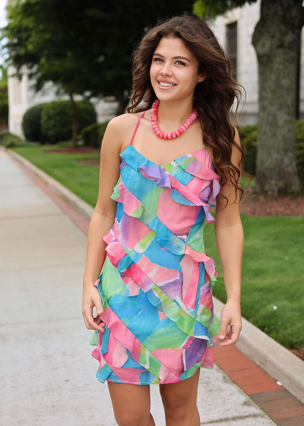 Woman wearing a colorful dress with ruffles on a sidewalk.