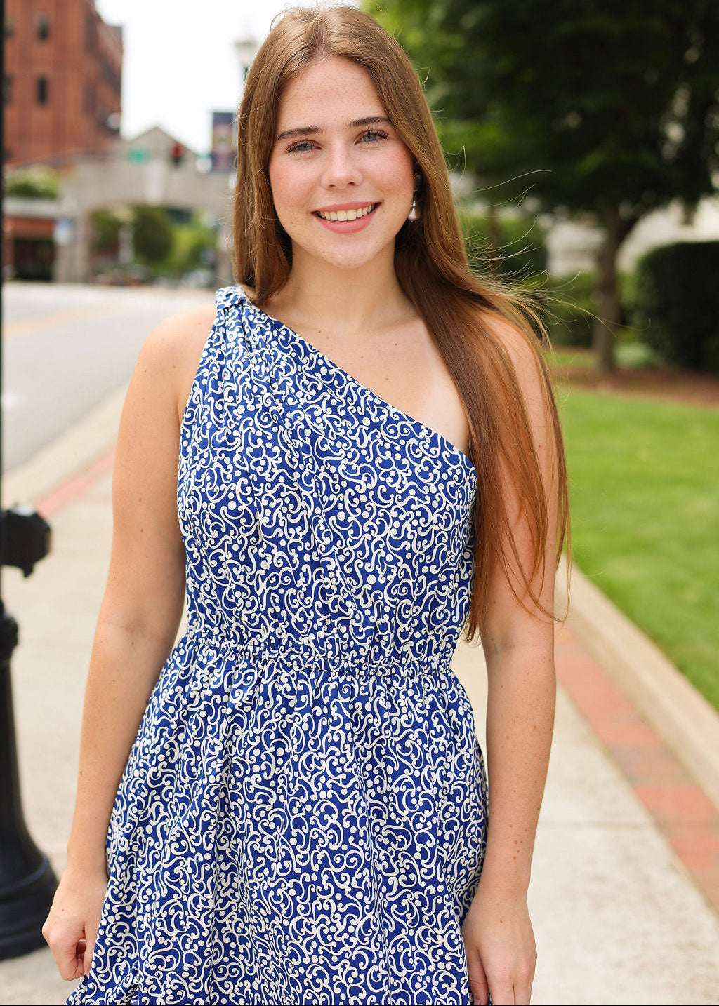 Woman in a blue floral dress standing outdoors on a sidewalk.