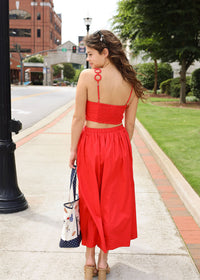 Woman in a red dress walking on a sidewalk with buildings and trees in the background