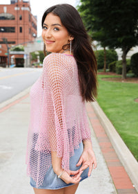 Woman wearing a pink knitted cover-up on a city street.