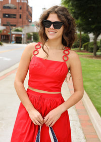 Woman in a red outfit with sunglasses standing on a sidewalk.