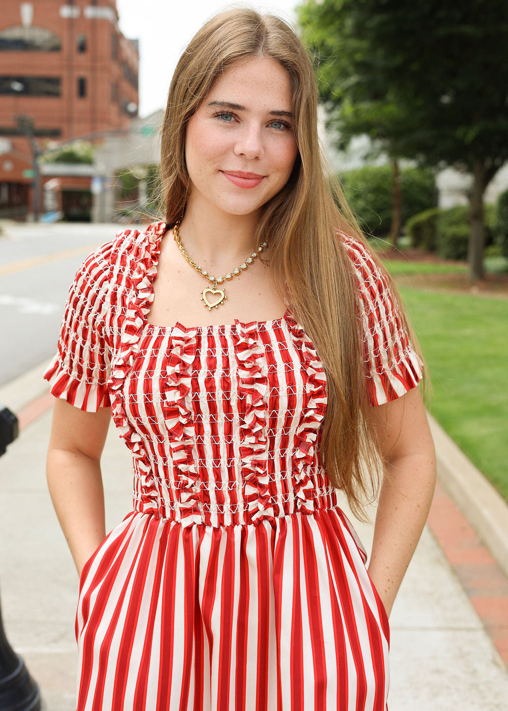 Woman wearing a red and white striped dress with a heart-shaped necklace outdoors.