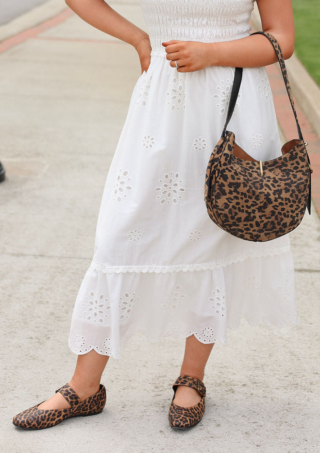 Woman in a white dress with a leopard print handbag and shoes on a city street.