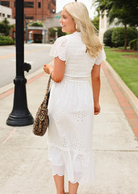 Woman in a white dress walking on a sidewalk holding a leopard print bag.