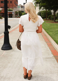 Woman in a white dress walking on a sidewalk with a leopard print handbag.