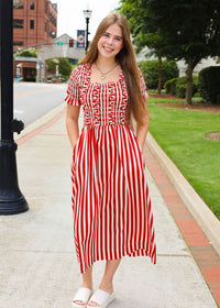 Woman in a red and white striped dress standing on a sidewalk with a city street in the background.