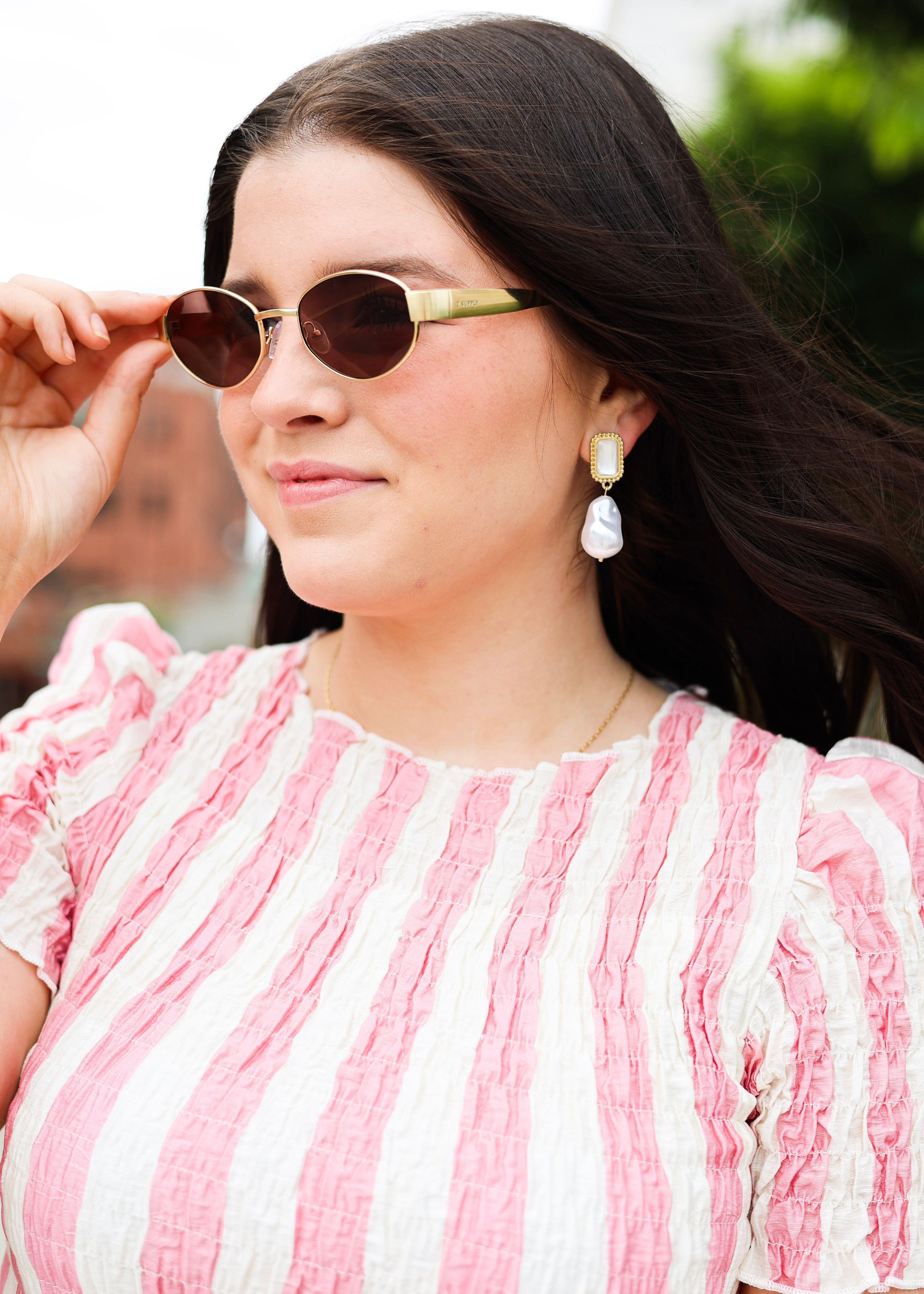 Woman wearing a pink and white striped dress with sunglasses and earrings outdoors.
