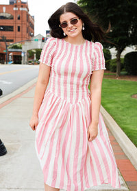 Woman wearing a pink and white striped dress on a city street.