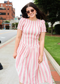 Woman wearing a pink and white striped dress on a sidewalk.