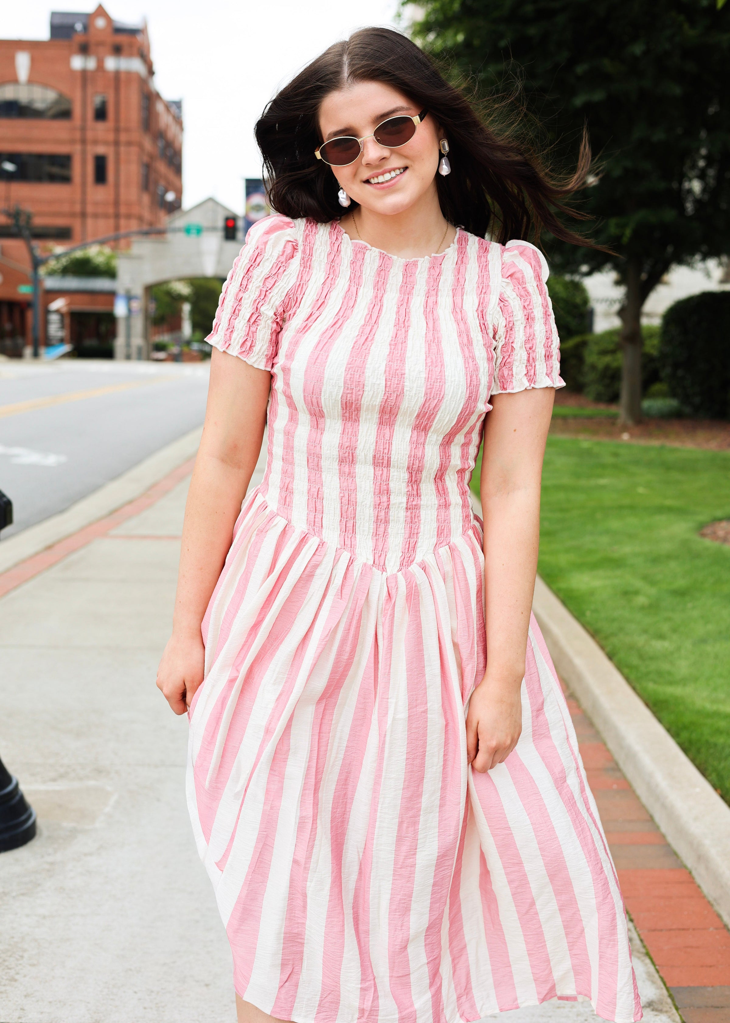 Woman wearing a pink and white striped dress on a sidewalk.