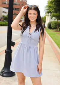 Woman in a light blue dress standing on a sidewalk with a building and trees in the background