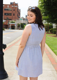 Woman in a light blue dress standing on a sidewalk with buildings and trees in the background