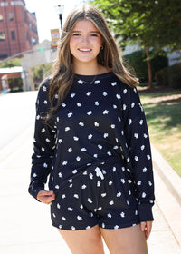 A young woman smiling outdoors while wearing a navy blue long-sleeve romper with a white all-over floral pattern.
