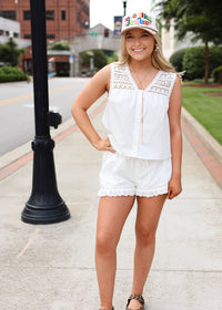 Woman in a white outfit with lace details standing on a sidewalk.