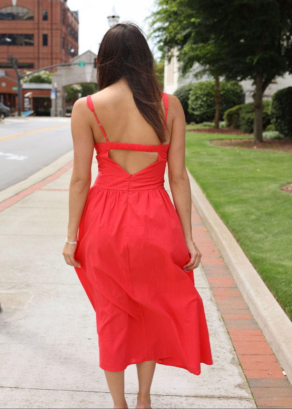 Woman wearing a red dress with an open back on a sidewalk.