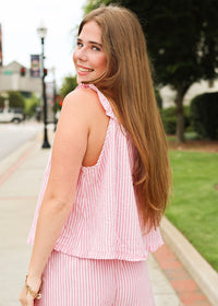 Woman wearing a pink striped outfit standing on a sidewalk with greenery in the background