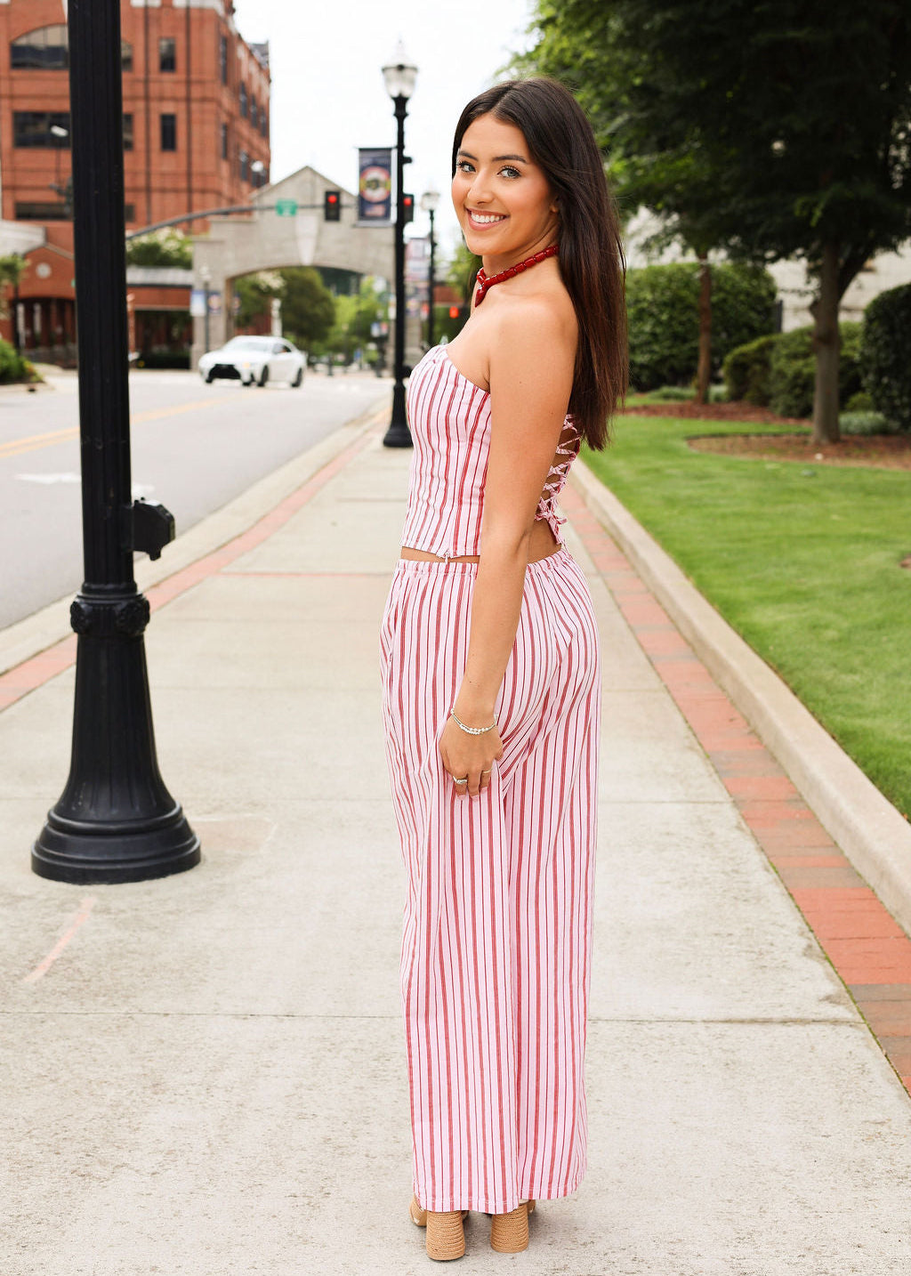 Woman in a red and white striped matching set standing on a sidewalk with buildings and trees in the background
