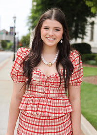 Woman wearing a red and white checkered dress with a pearl necklace outdoors.