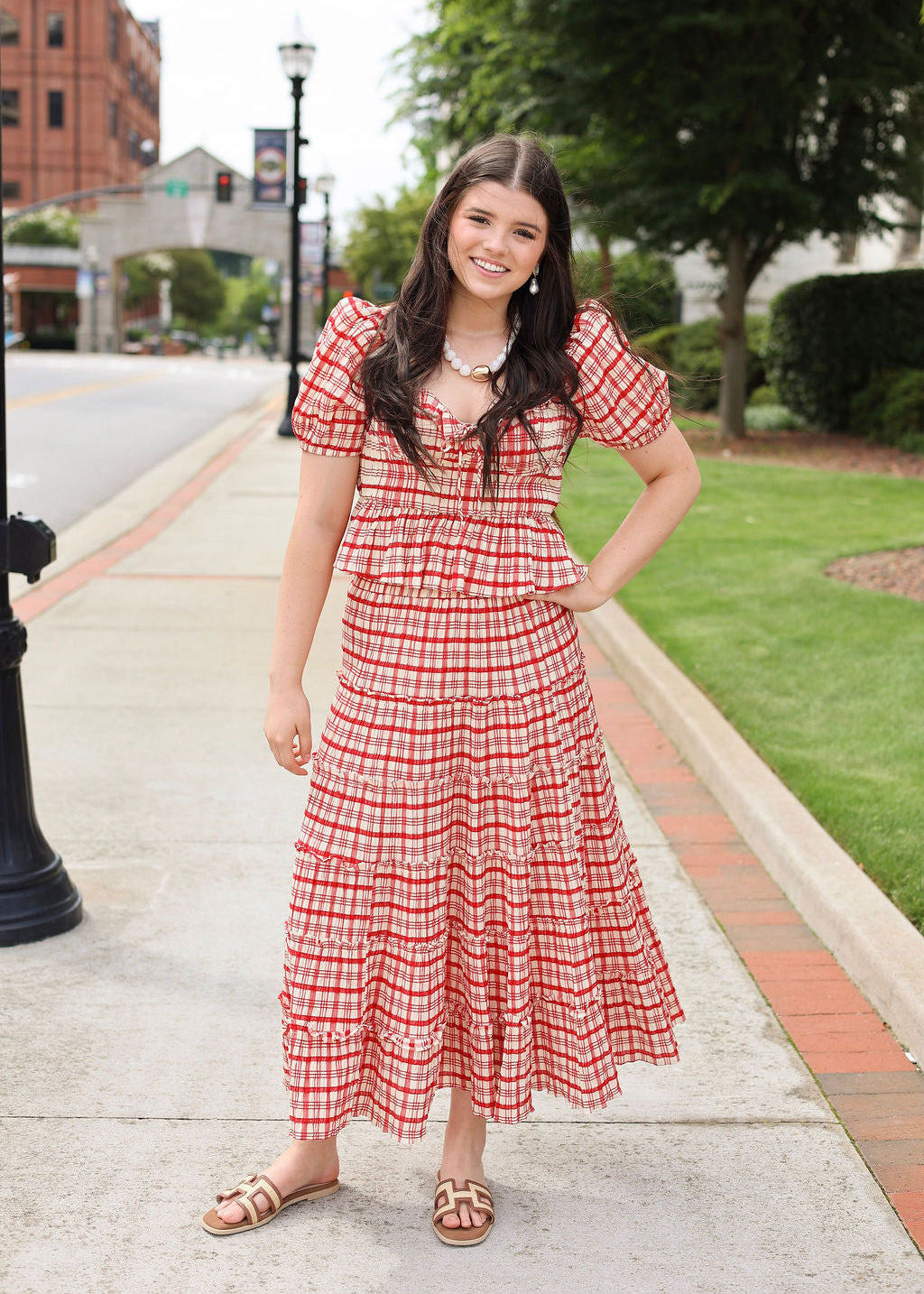 Woman in a red checkered dress standing on a sidewalk with a city street background