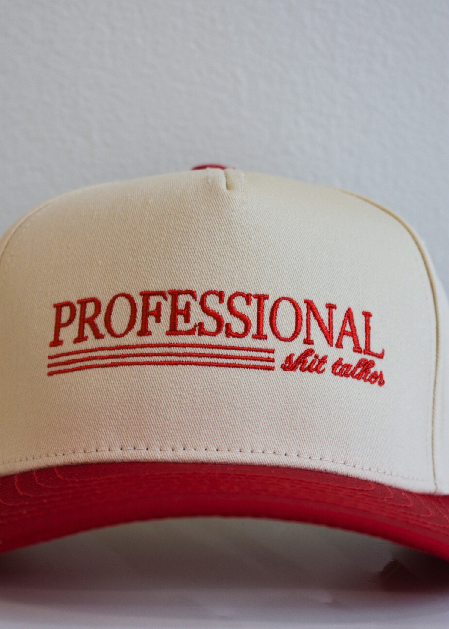 Close up of Professional Shit Talker embroidery on red and natural snapback hat