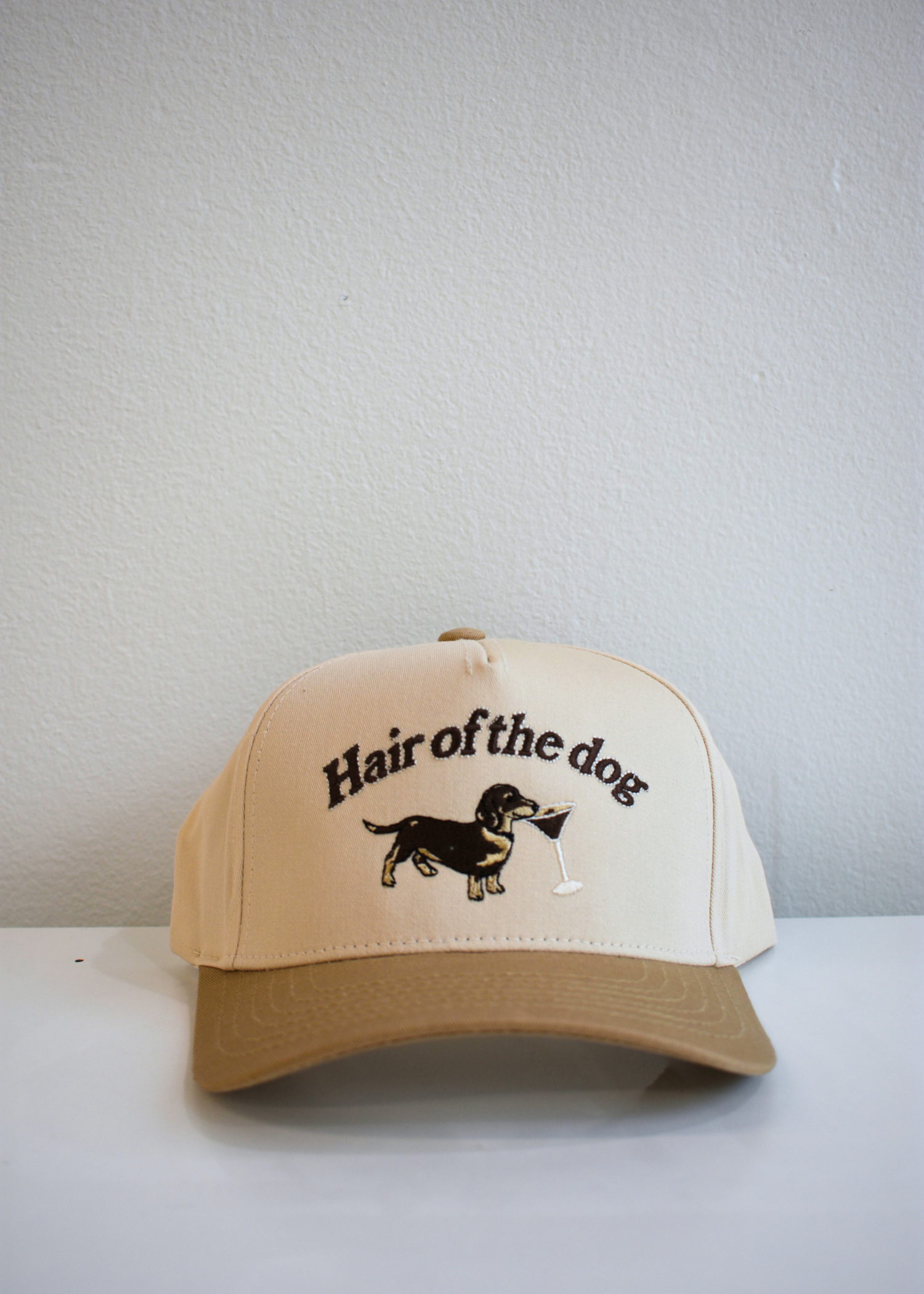 Front view of Hair of the Dog tan and natural trucker hat featuring dachshund and espresso martini embroidery